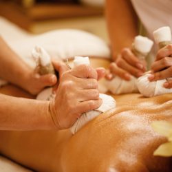 Close-up of two therapists massaging back of a customer with herbal compress at the spa.